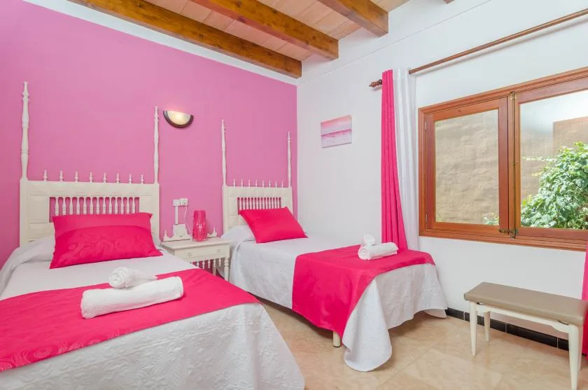 A bright bedroom with two beds dressed in pink and white linens.