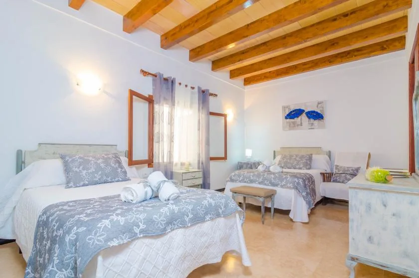 A bright bedroom with two beds, a small table, and exposed wooden ceiling beams.