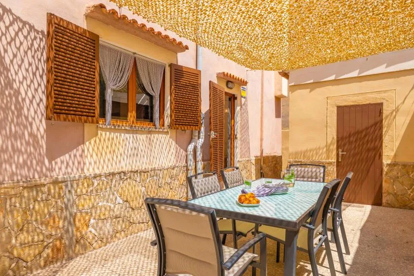 An outdoor dining area has a glass-topped table and seating beside a house.
