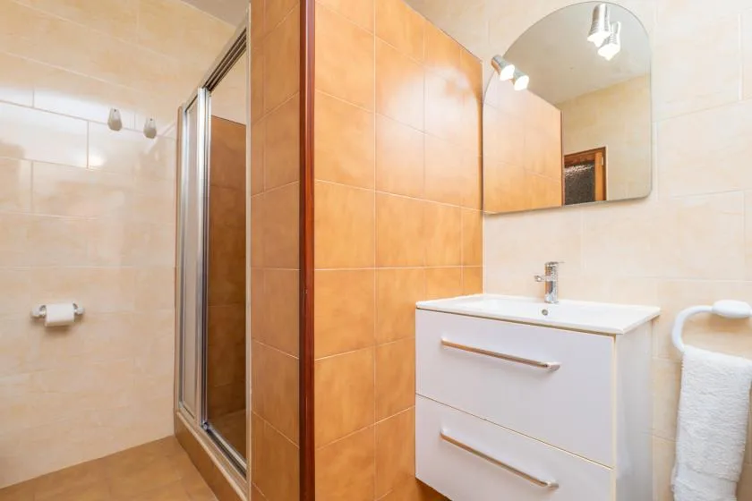 A tiled bathroom with a glass shower, sink vanity, and wall mirror.