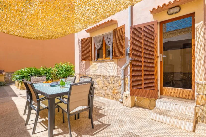 Un patio soleado con asientos al aire libre y una puerta abierta bajo un toldo.