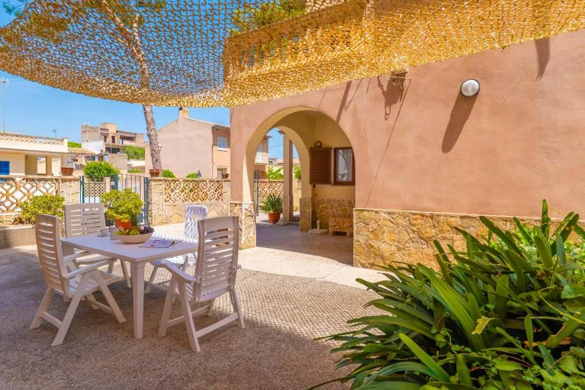 An outdoor patio has a dining table and chairs beneath a woven shade canopy.