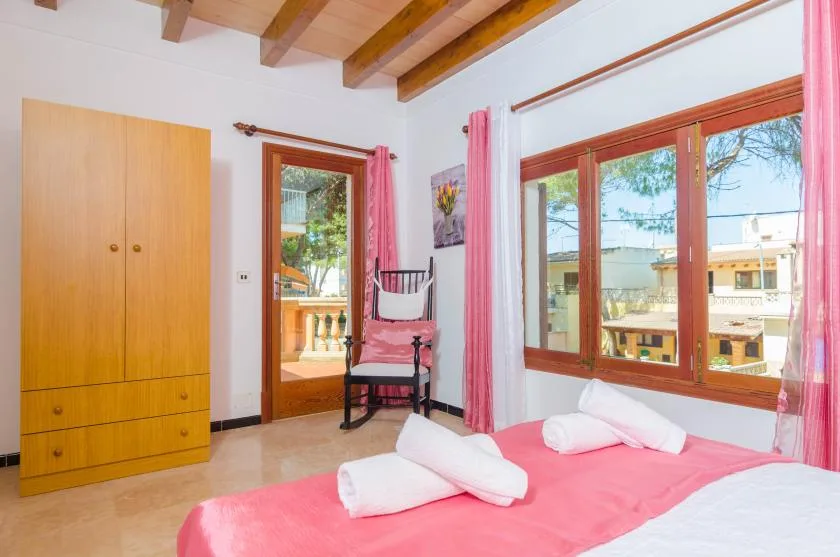A bedroom with a pink bedspread, wooden wardrobe, and large windows.