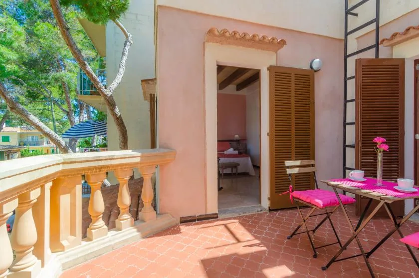 A sunny terrace with outdoor seating overlooks leafy trees and an open doorway.