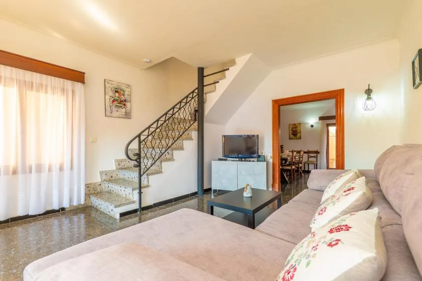 A living room with seating, a coffee table, and a staircase beside a curtained window.