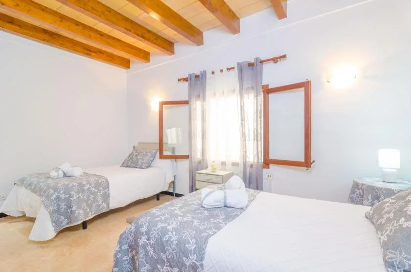 A bright bedroom with two beds and a window between them.