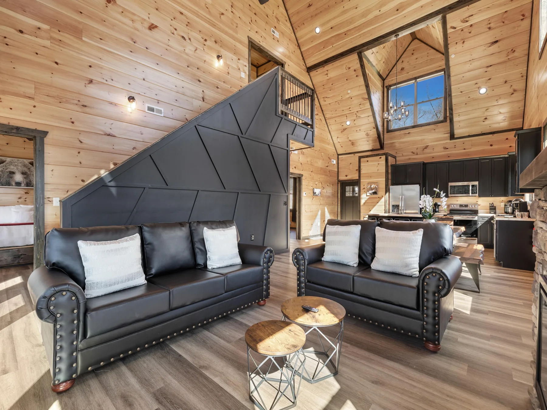 A wood-paneled living room with two dark sofas and a kitchen in the background.