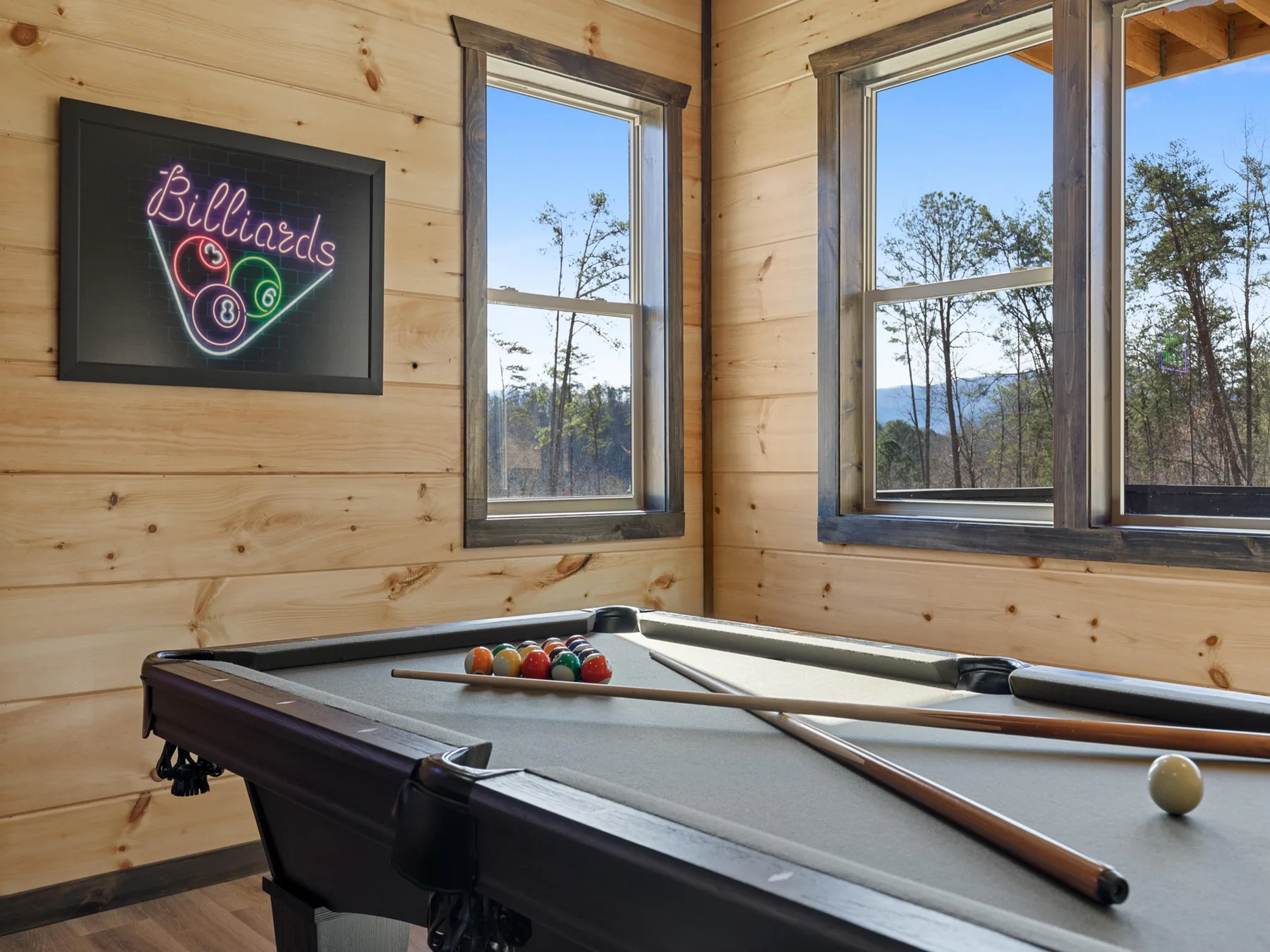 A billiards table sits beside large windows in a wood-paneled game room.