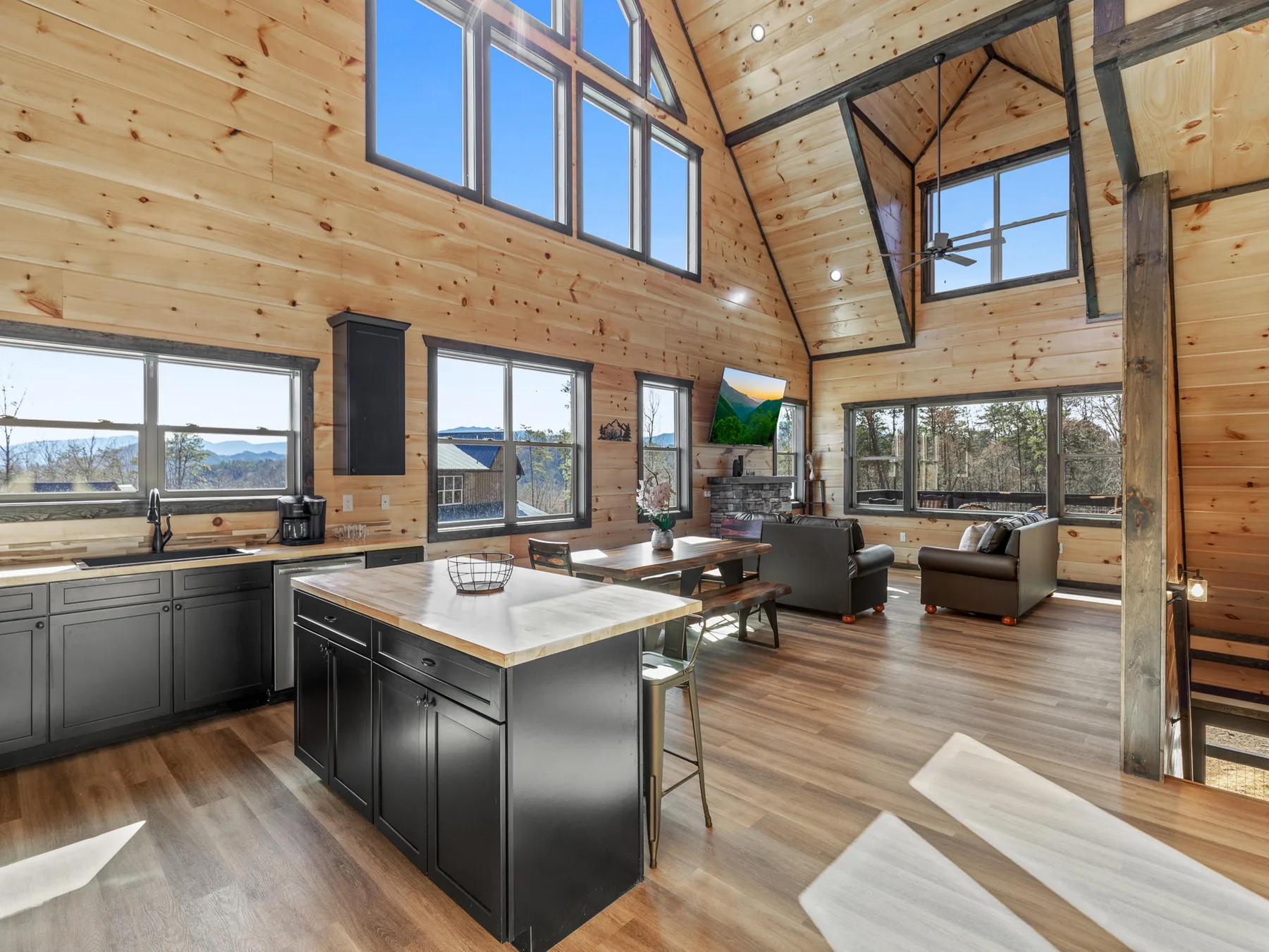 A spacious wood-paneled living room and kitchen with large windows and an island.