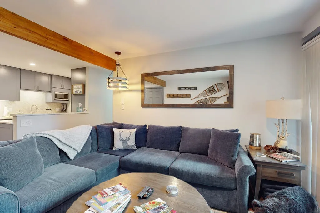 A living room with an L-shaped seating area, coffee table, and open kitchen.