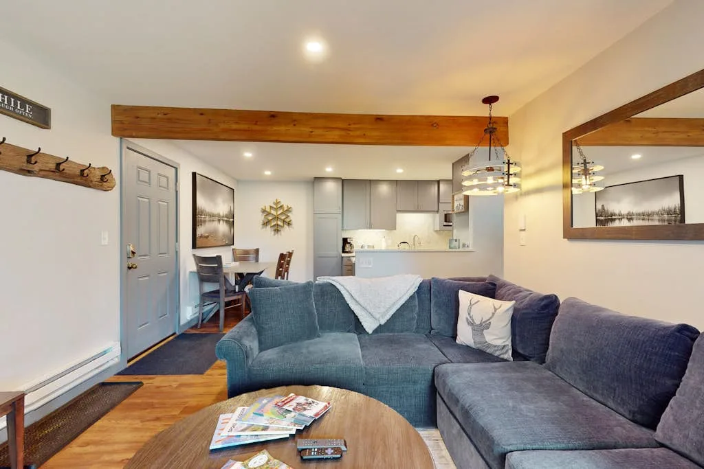 A living room with sectional seating and an open kitchen in the background.