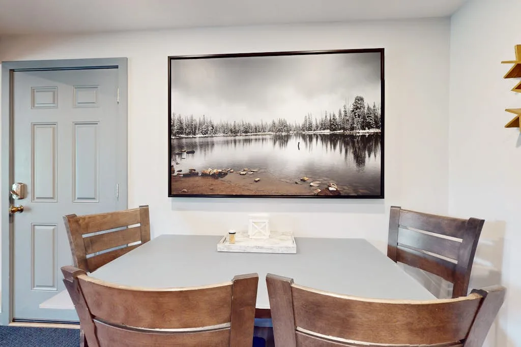 Un comedor con una mesa rectangular, asientos de madera y una gran imagen de paisaje.
