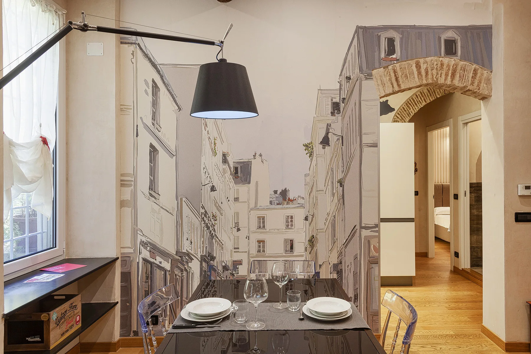 Comedor con la mesa puesta, paredes con un mural y una puerta abierta.