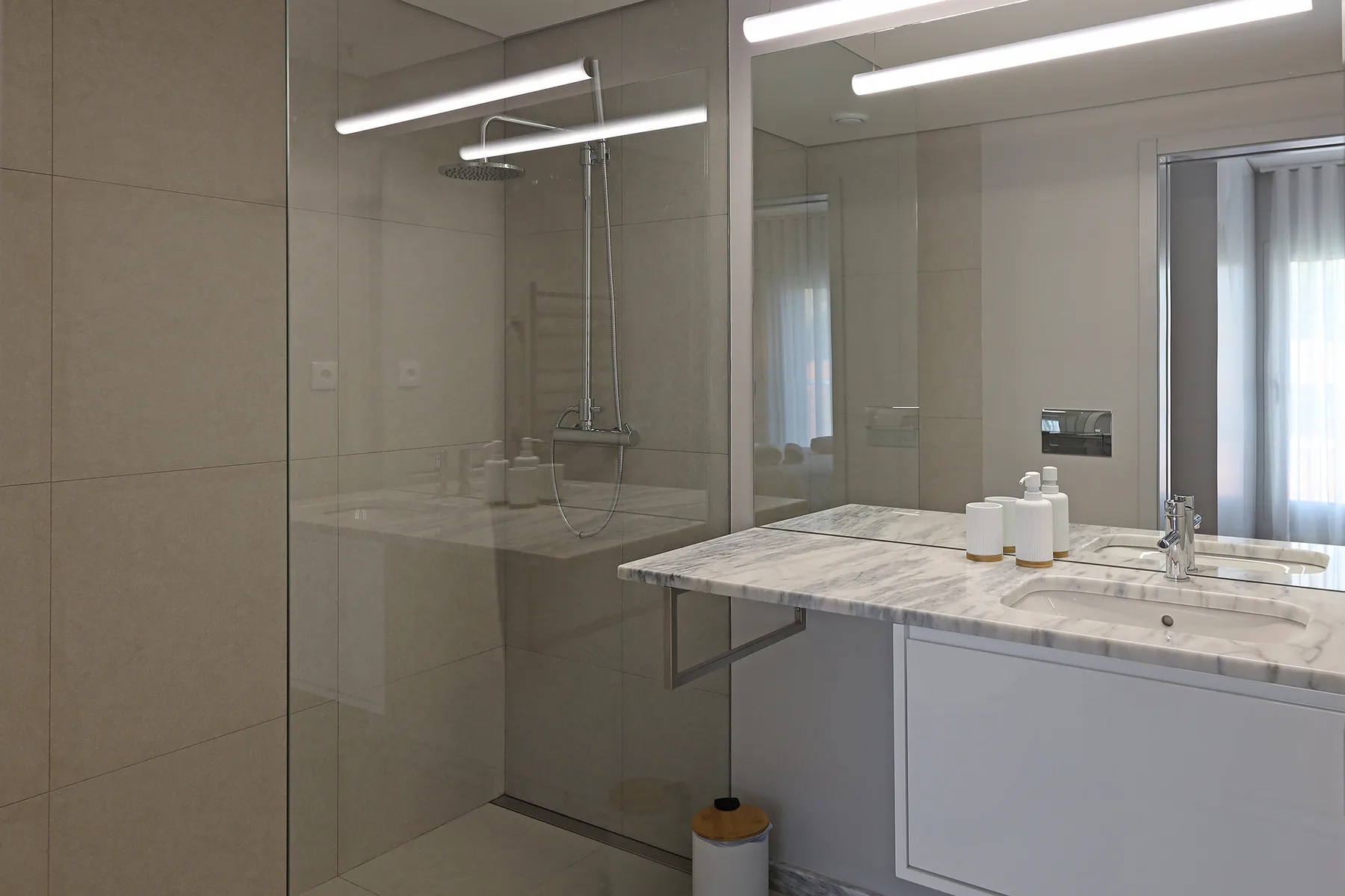 A bathroom vanity with a wide mirror and a glass shower.