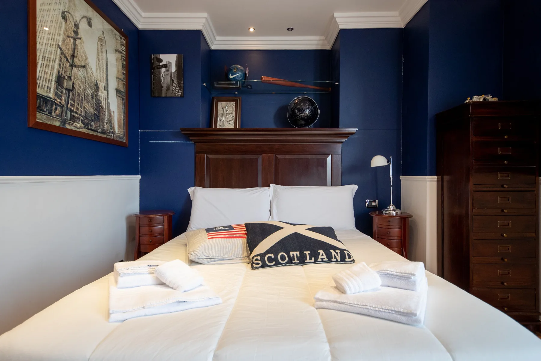 Un dormitorio con una cama bien tendida, paredes azul oscuro y un cabecero de madera.