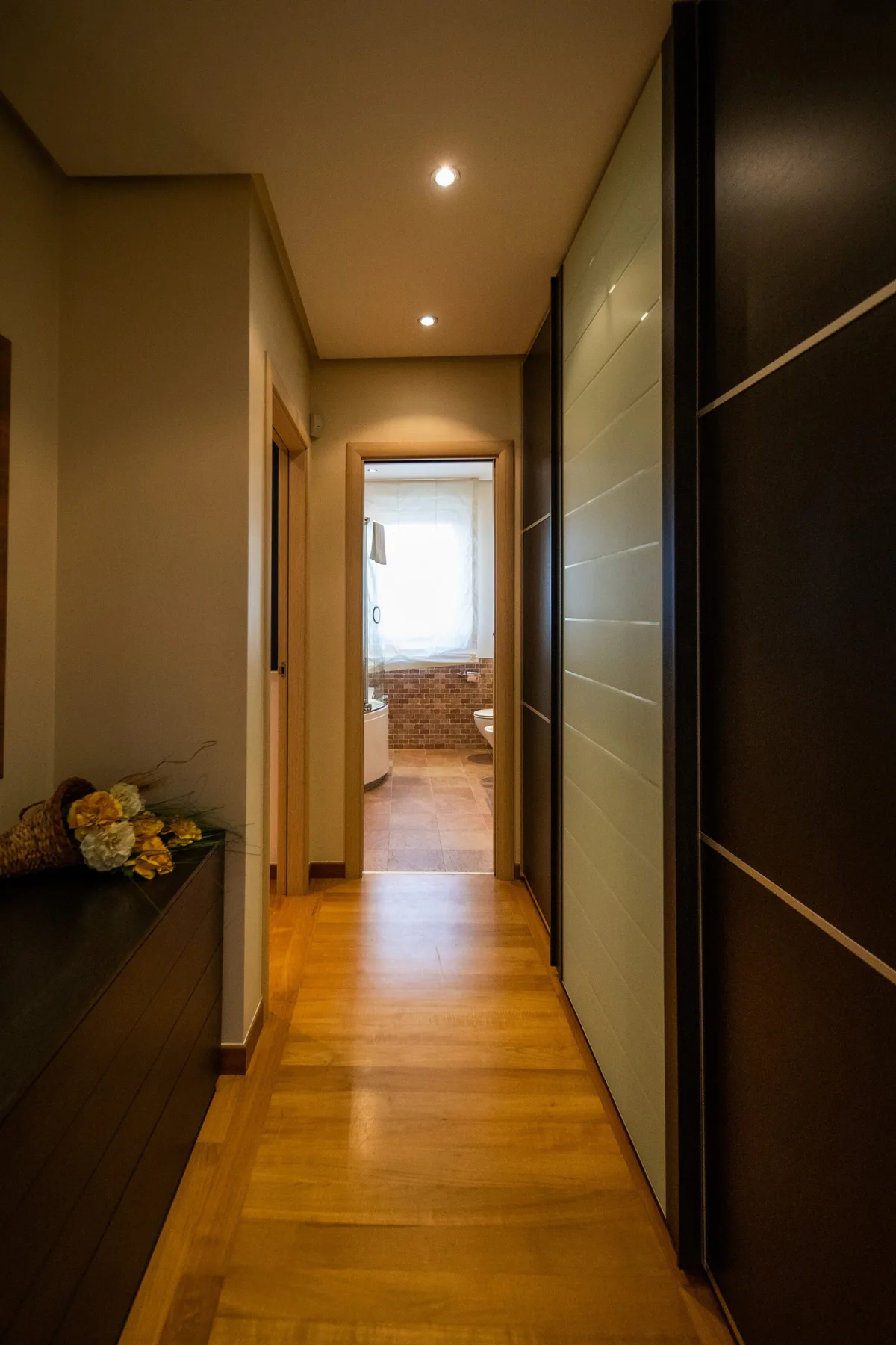 A hallway leads to a bathroom with a bright window at the far end.