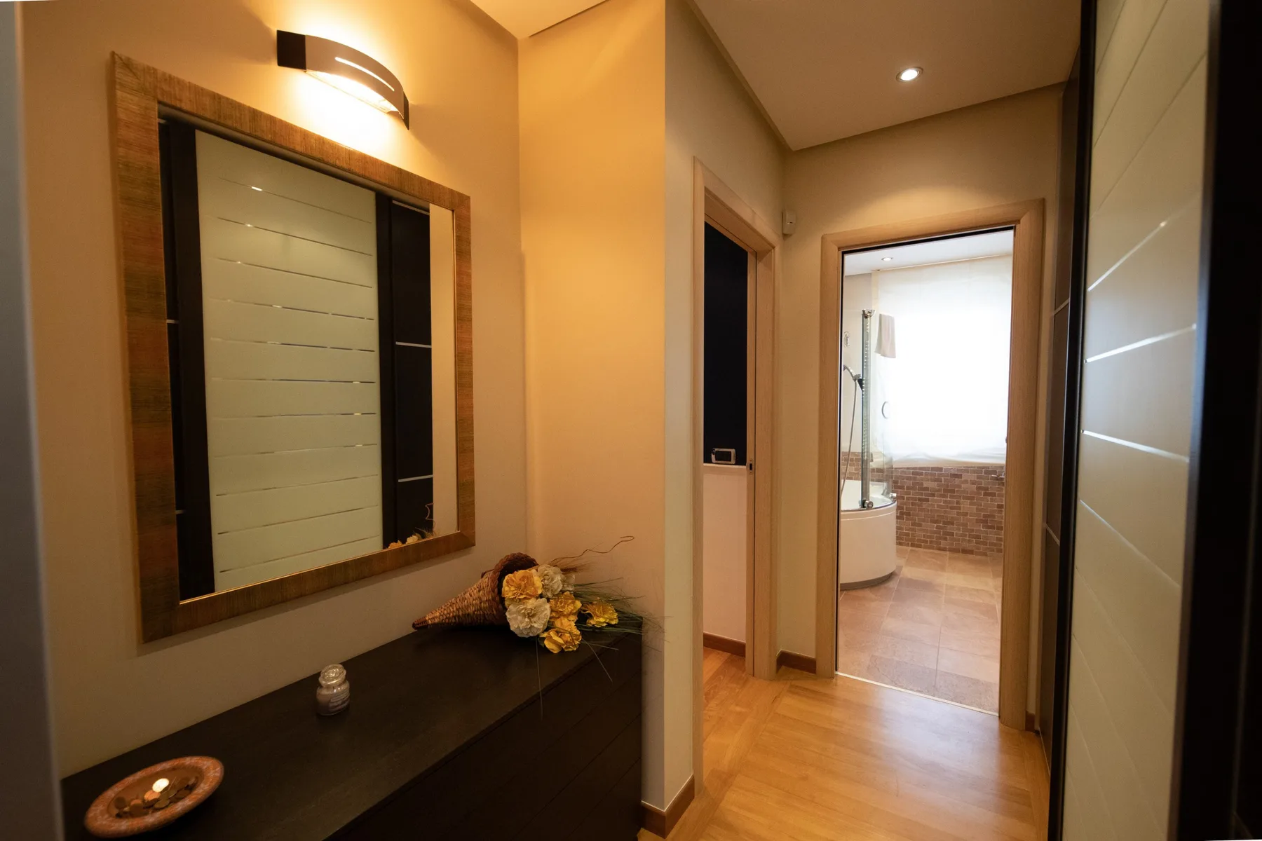 A warm-toned hallway with a wall mirror and a doorway to a bathroom.