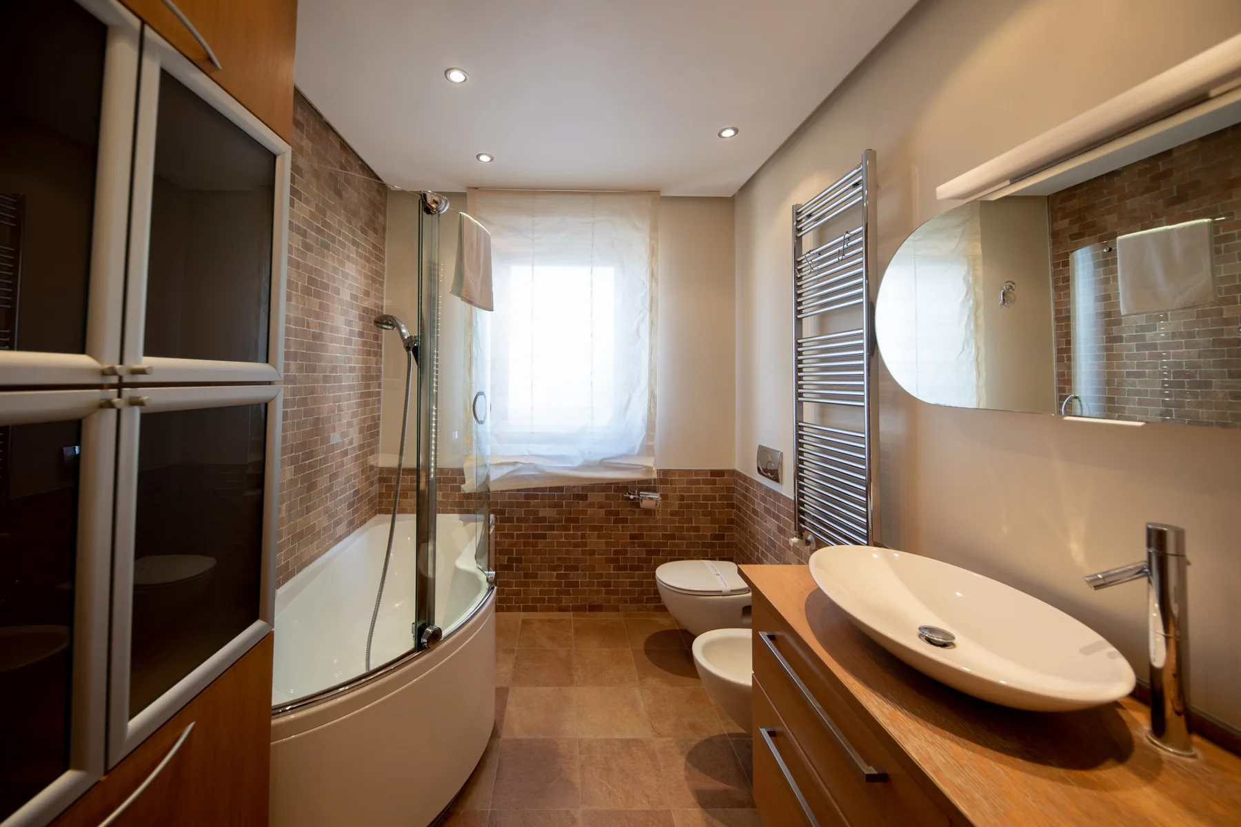 A bathroom with a curved shower, bathtub, toilet, and vanity.