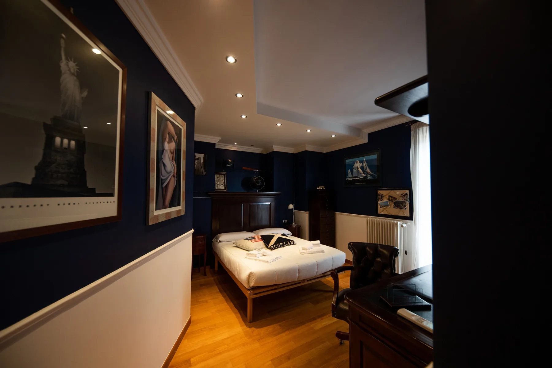 A bedroom with a bed, dark walls, and framed artwork.