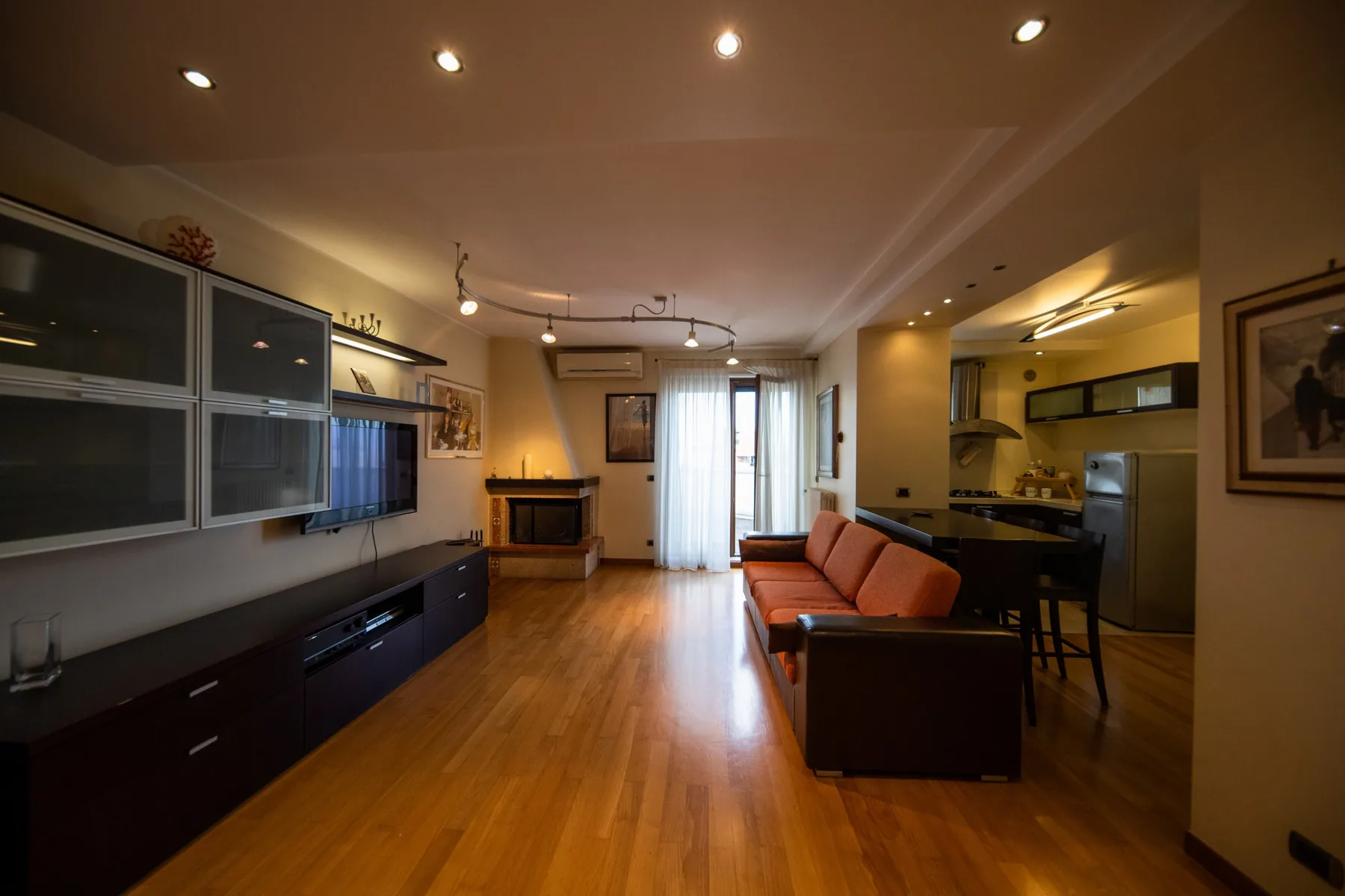 Una sala de estar con asientos, un televisor y una cocina abierta.