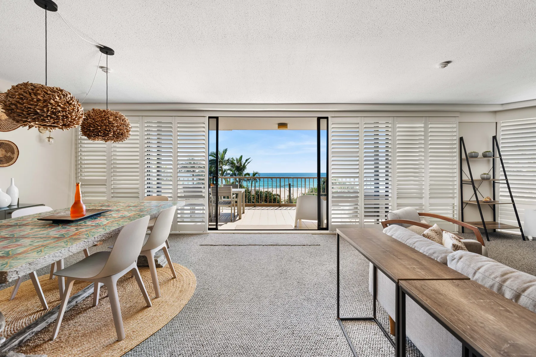 An open-plan living and dining room overlooks a balcony and the ocean.