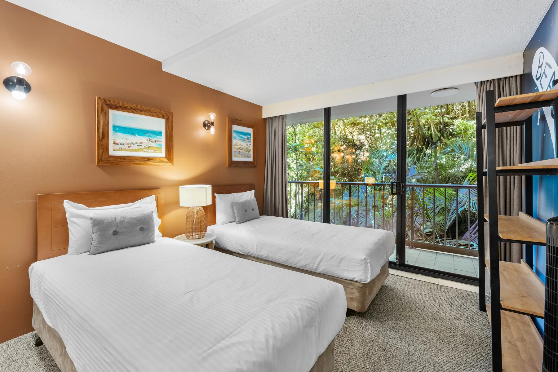 A bedroom with two beds beside a glass door opening onto leafy greenery.