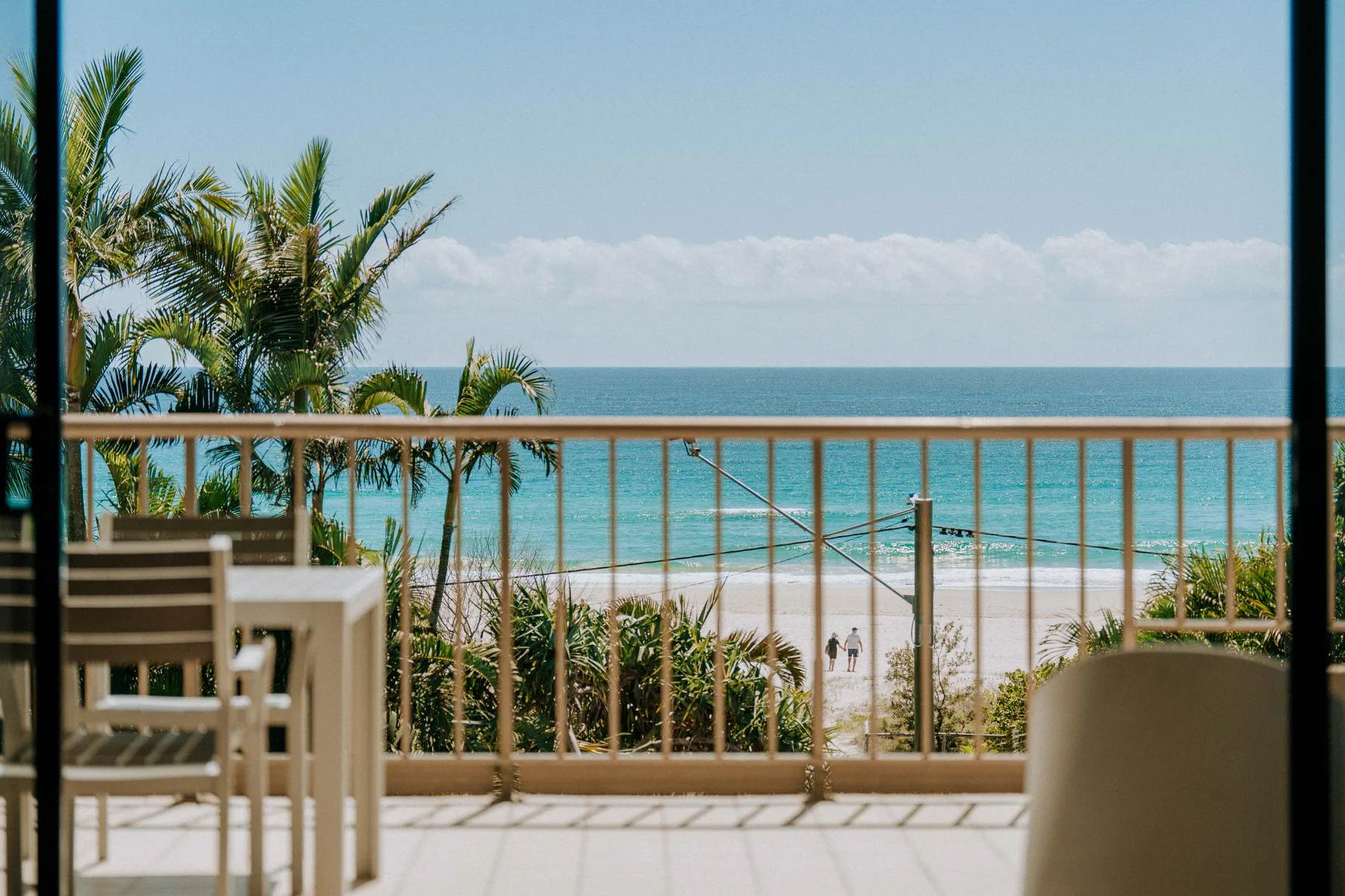 A balcony seating area overlooks the ocean and a sandy beach.