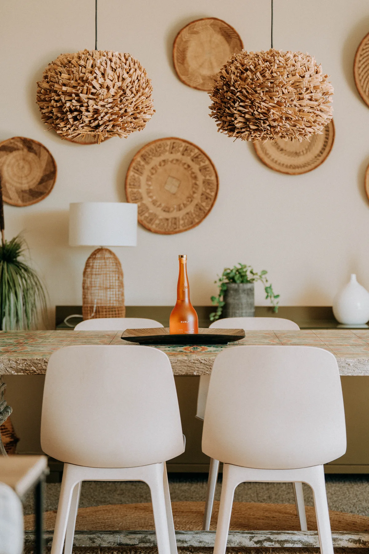 A dining area with a table, white seating, and woven wall decorations.