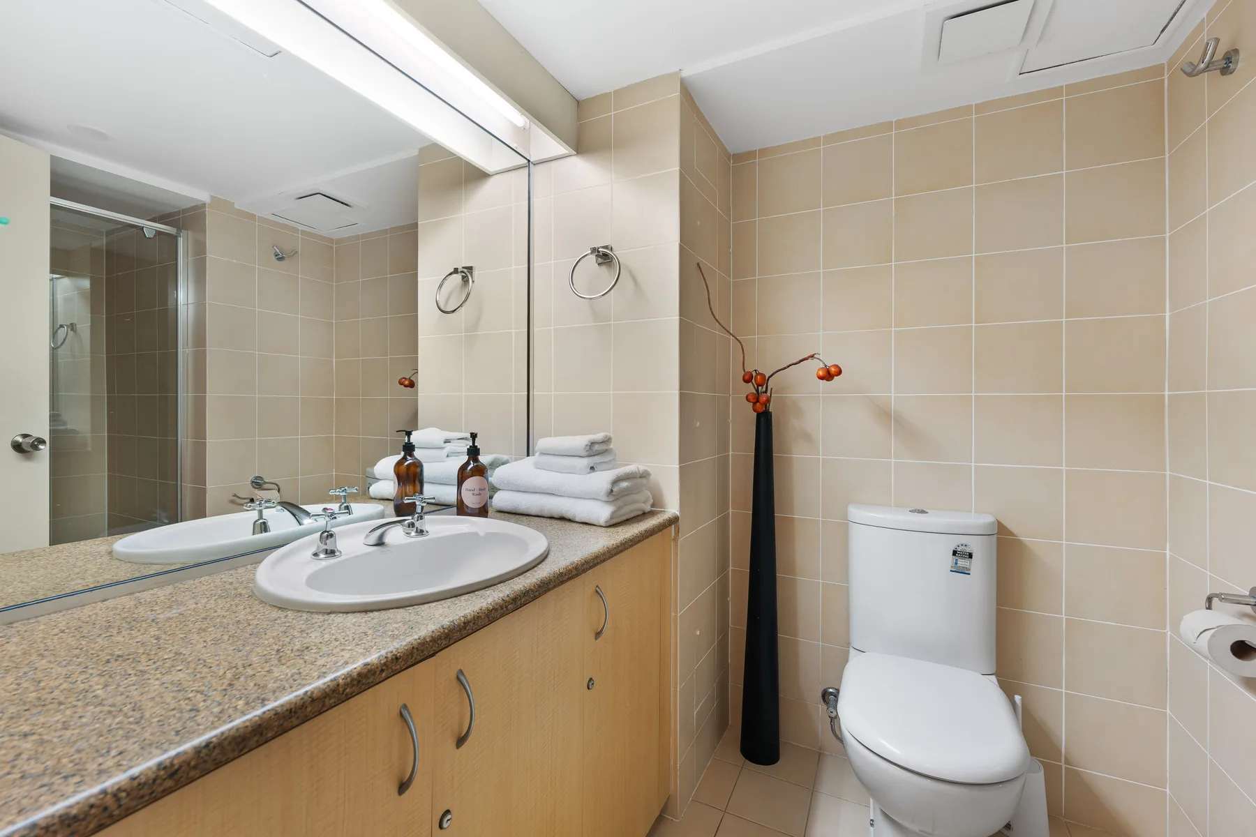 A tiled bathroom with a vanity, mirror, and toilet.