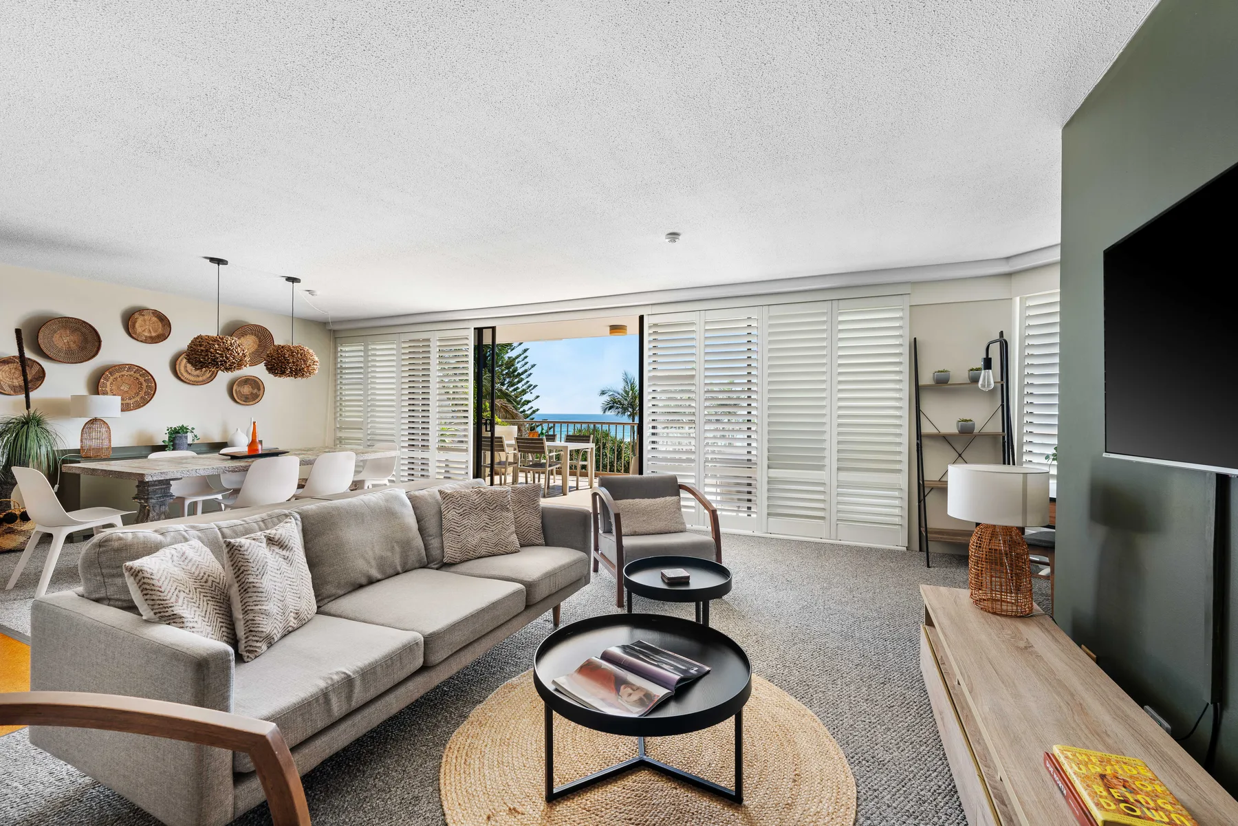 A bright living room with seating, a dining area, and a glimpse of the ocean.