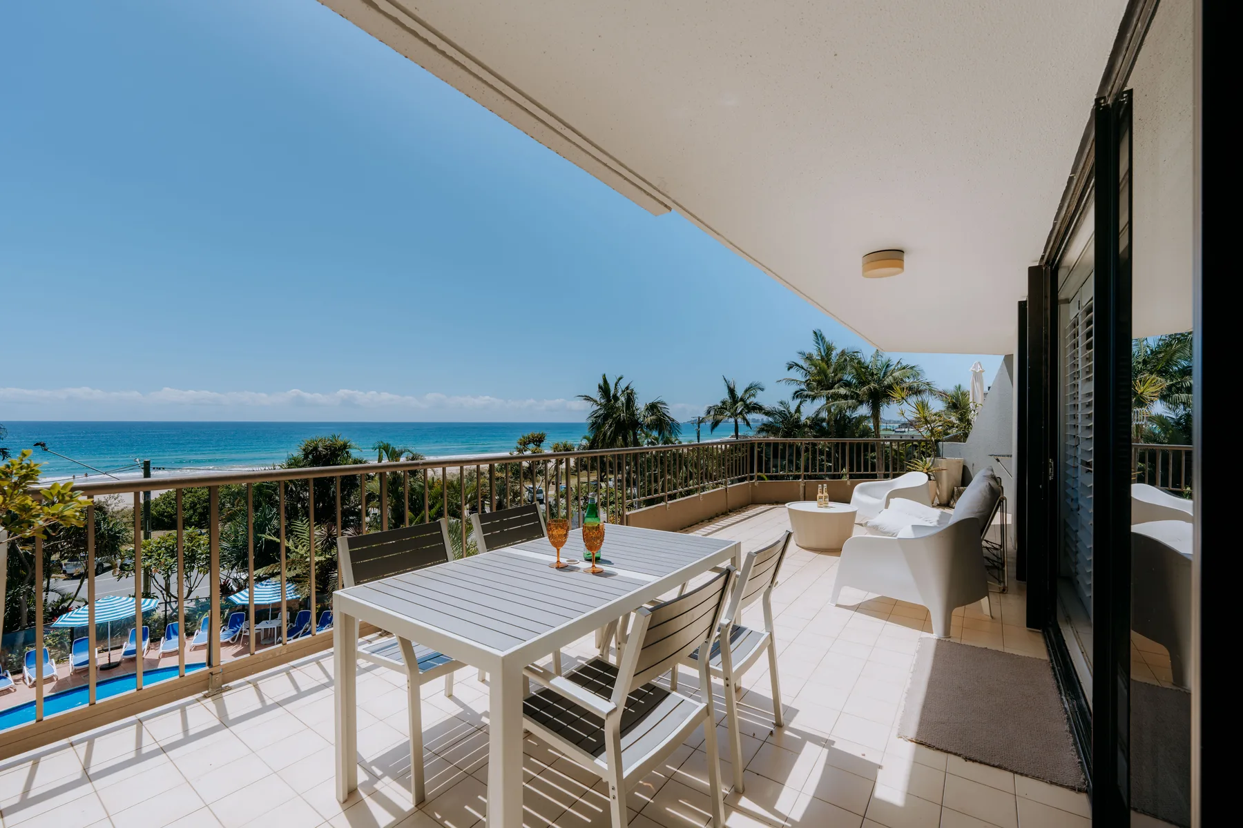 A balcony dining area overlooks the ocean and nearby palm trees.