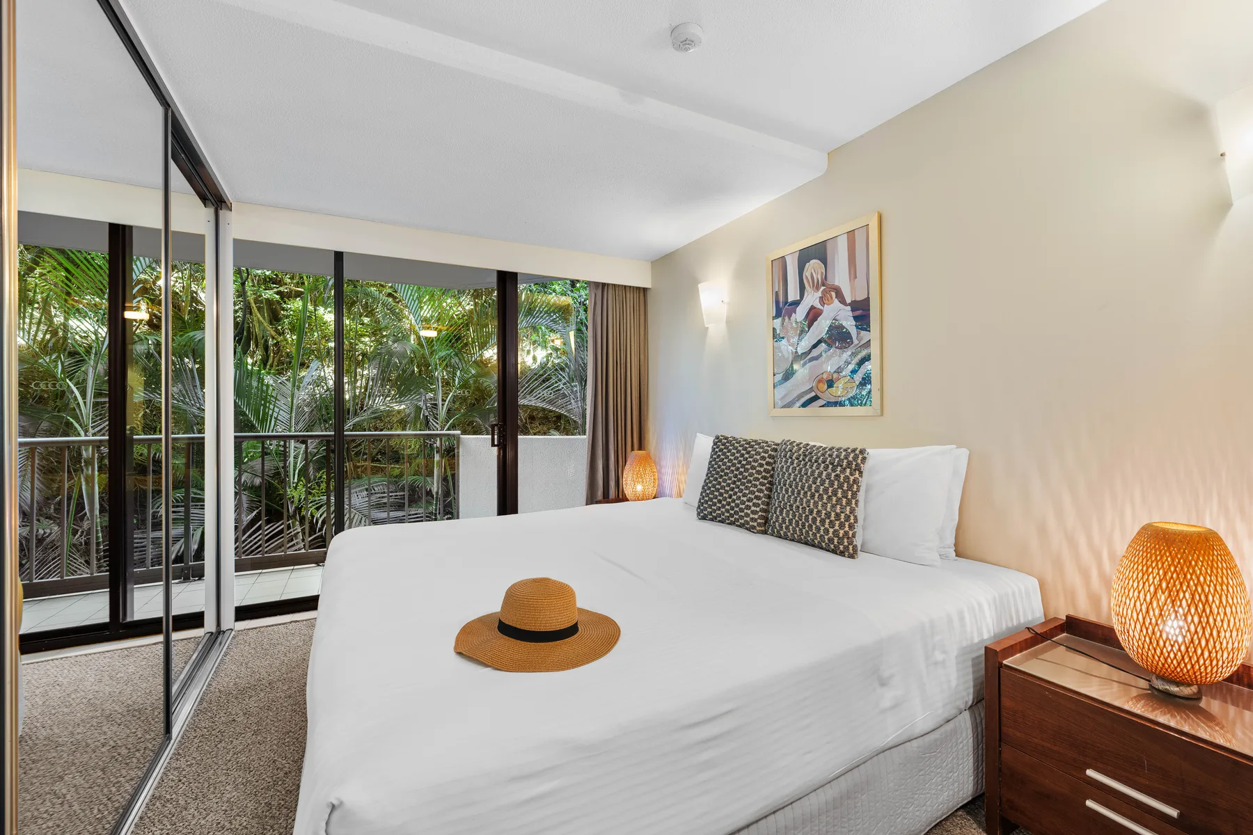 A bedroom with a neatly made bed beside large glass doors opening onto greenery.