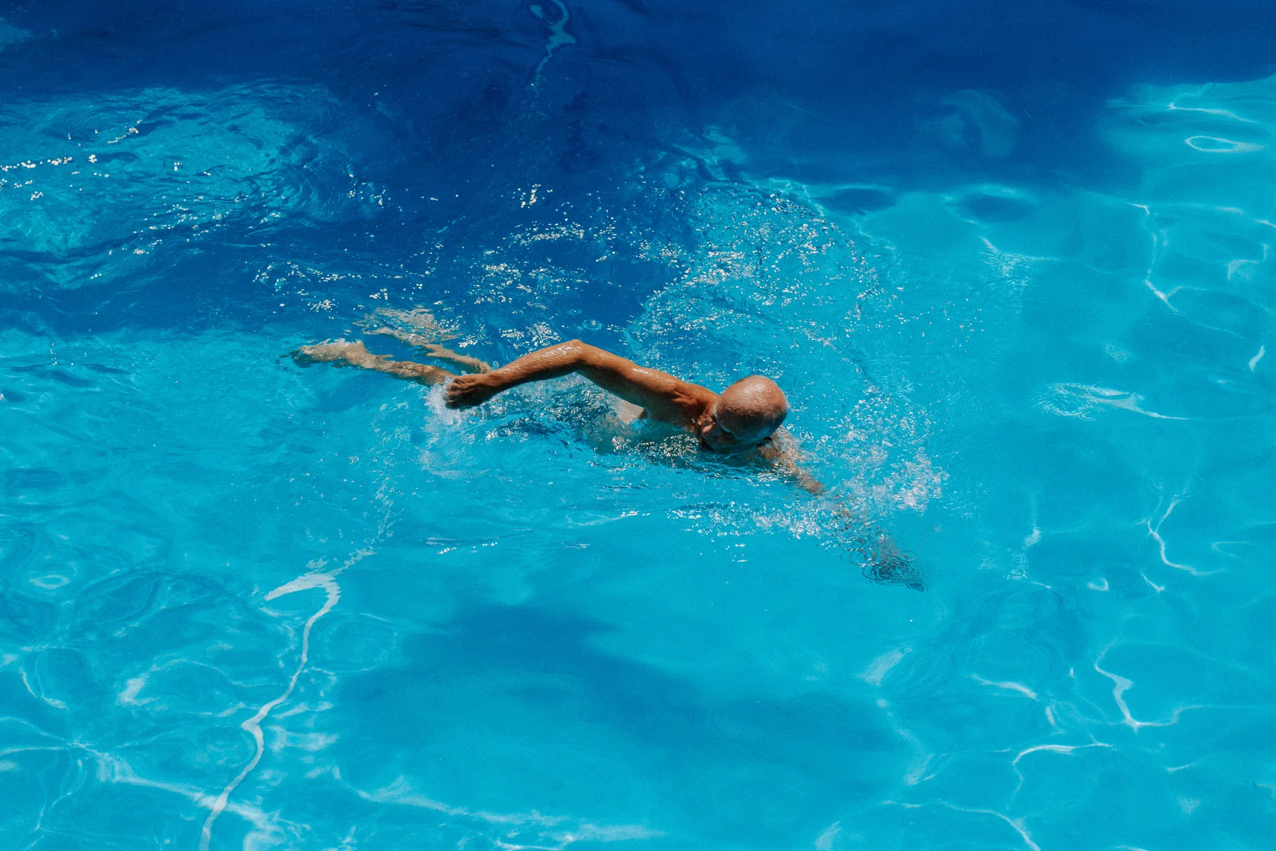 A swimmer moves through clear blue water in an outdoor pool.