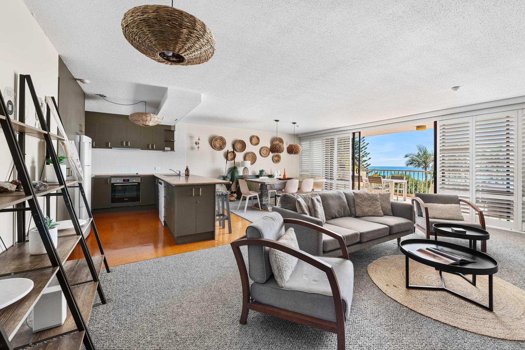 An open-plan living room and kitchen with seating beside windows overlooking the ocean.