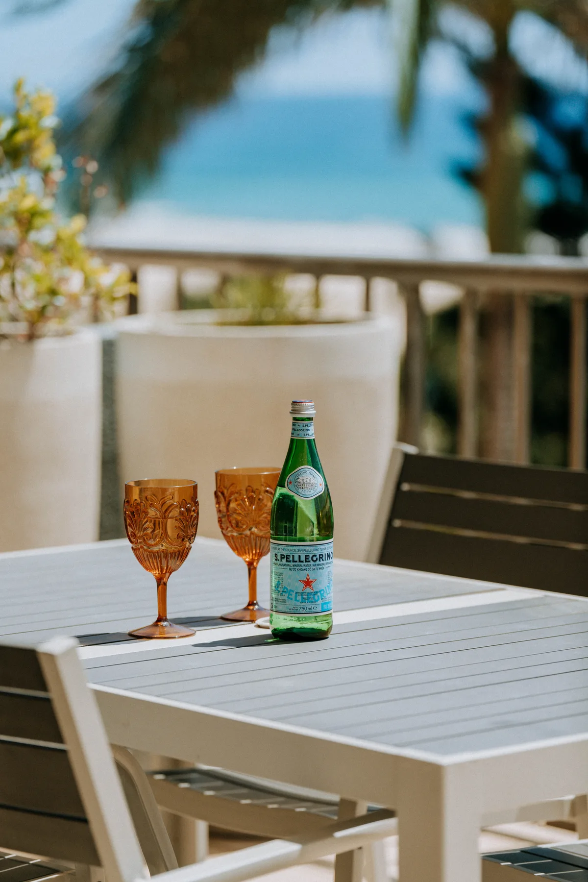 An outdoor dining area with amber glasses and a green bottle on the table.