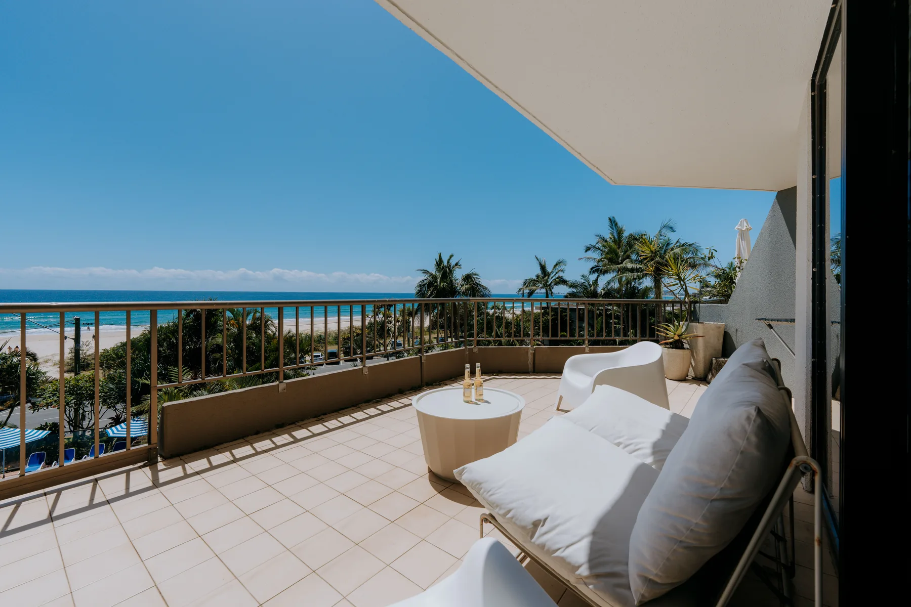 A tiled balcony with cushioned seating overlooks palm trees and the ocean.