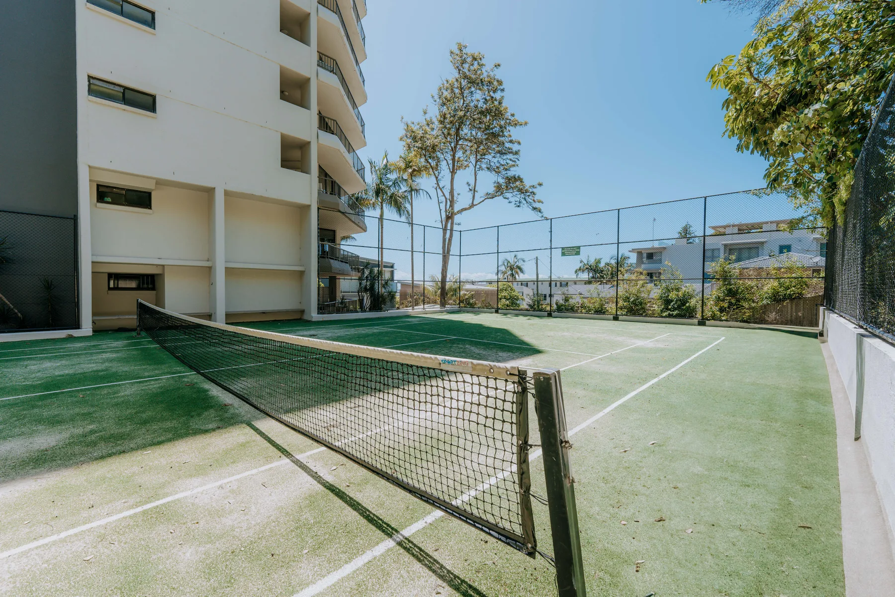 A tennis court with a net sits beside a multi-story building.
