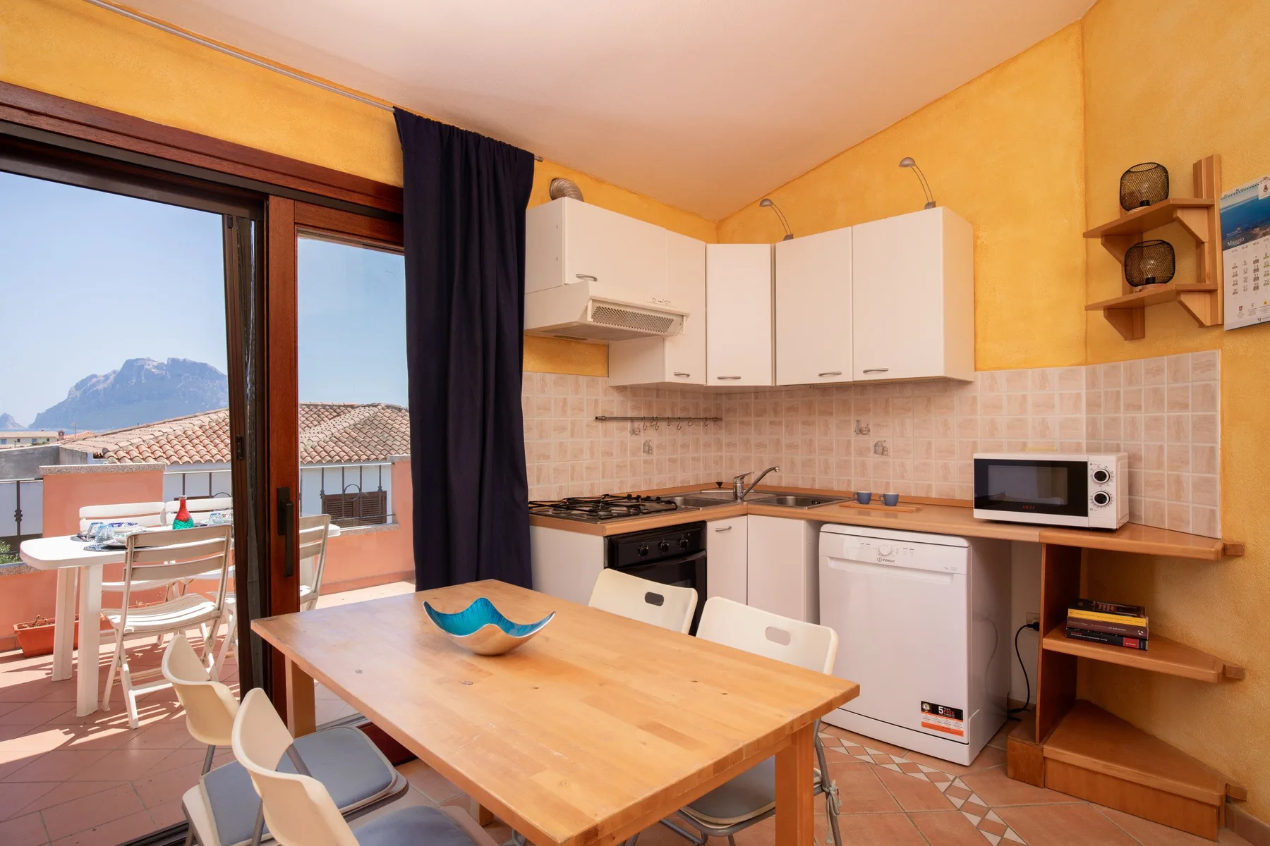 Una cocina compacta con zona de comedor se abre a un balcón mediante puertas correderas de cristal.