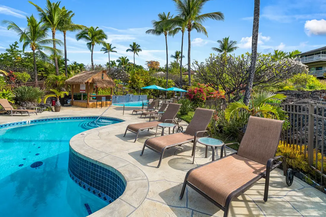 Una zona de piscina tropical al aire libre con tumbonas y palmeras.