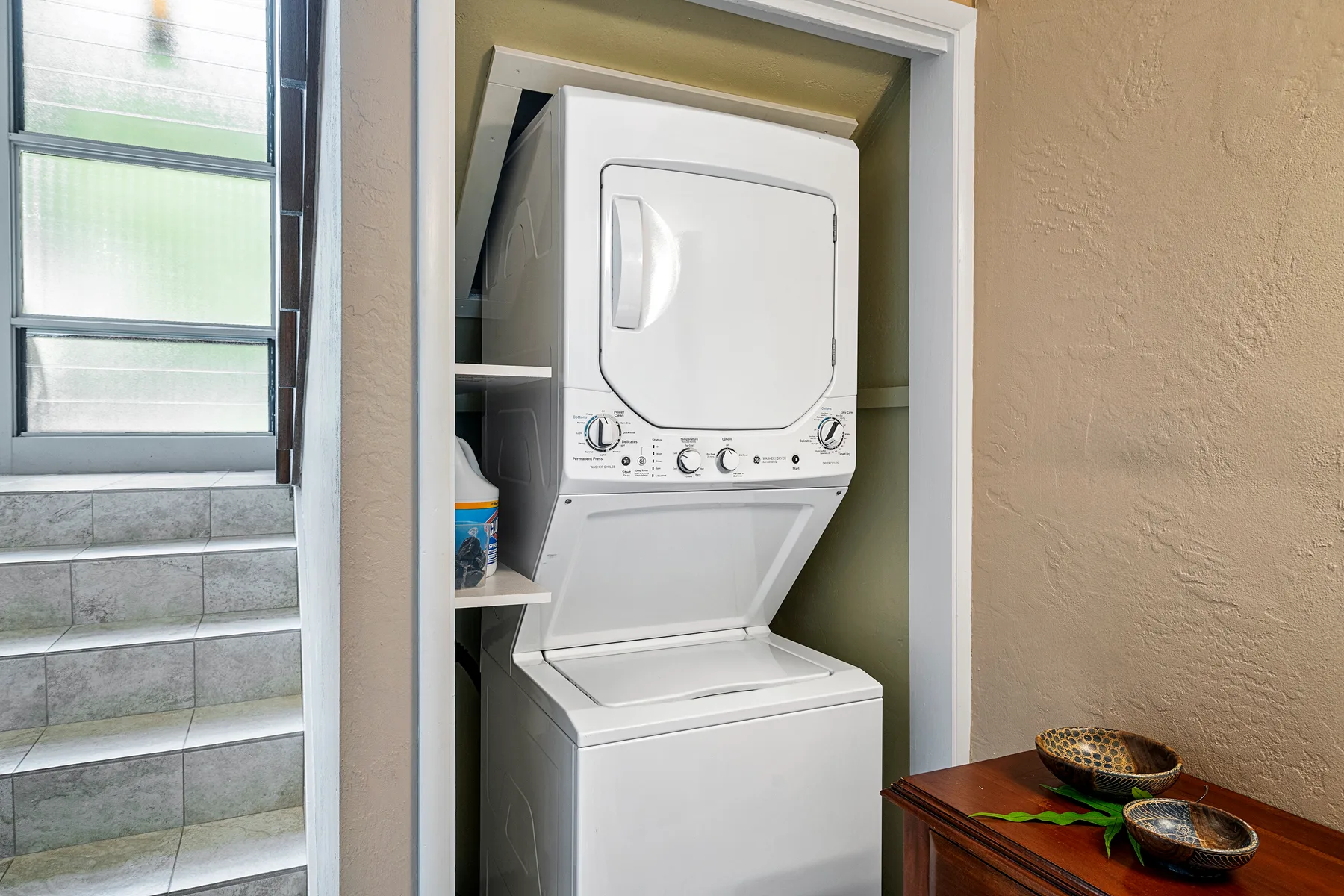 Zona de lavandería con lavadora y secadora apiladas junto a una ventana.