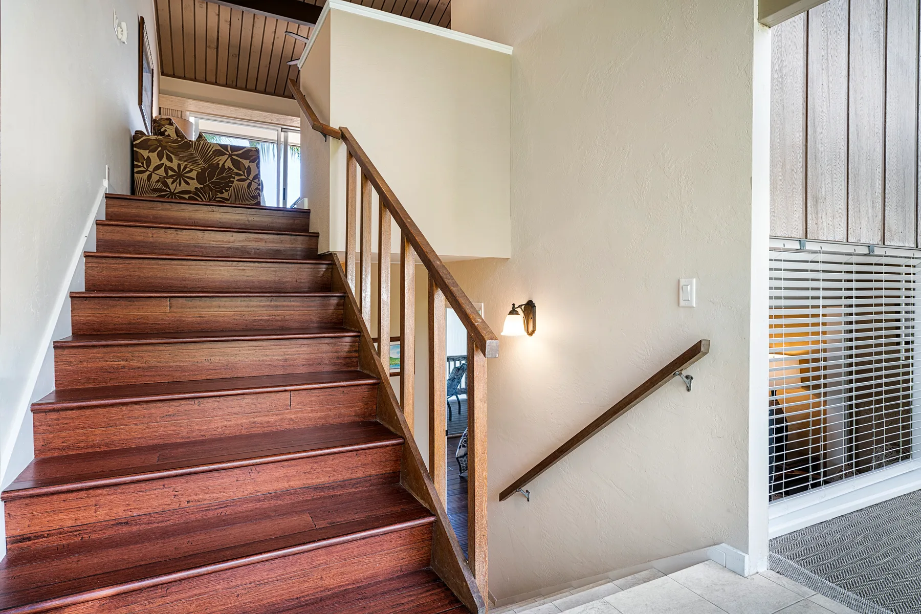 Una escalera de madera con pasamanos sube junto a una pared clara.