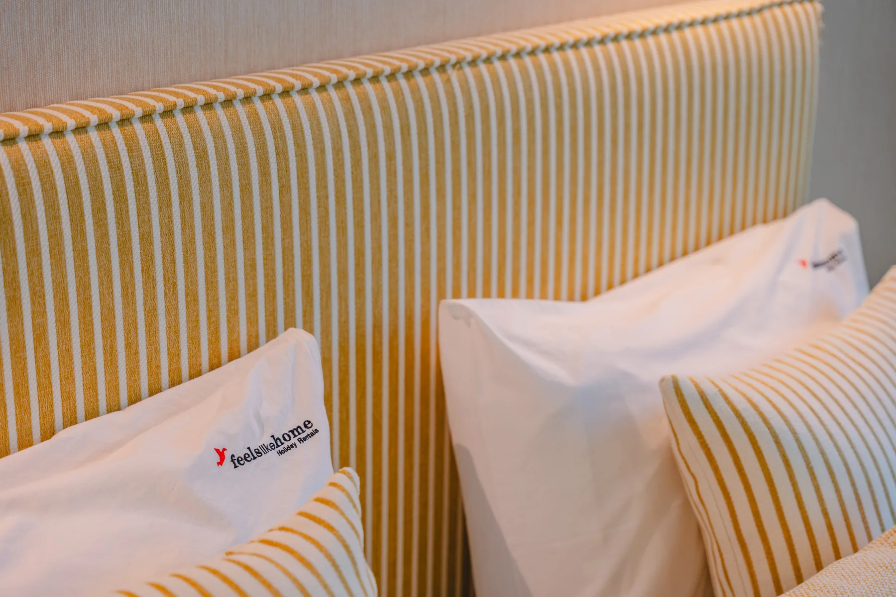 Una cama con almohadas blancas y ropa de cama a rayas amarillas y blancas.