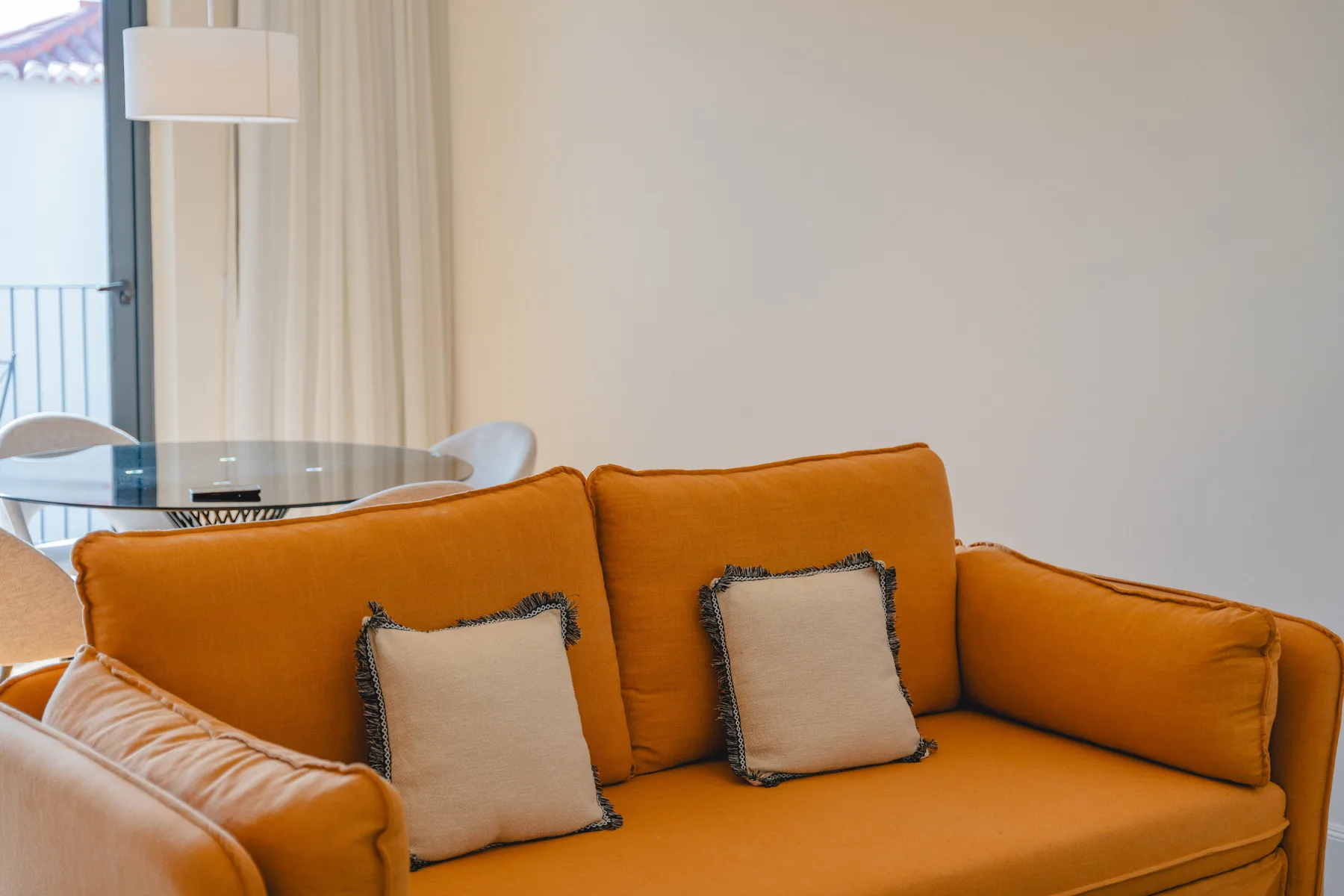 Una sala de estar con asientos naranjas y un pequeño comedor junto a la ventana.