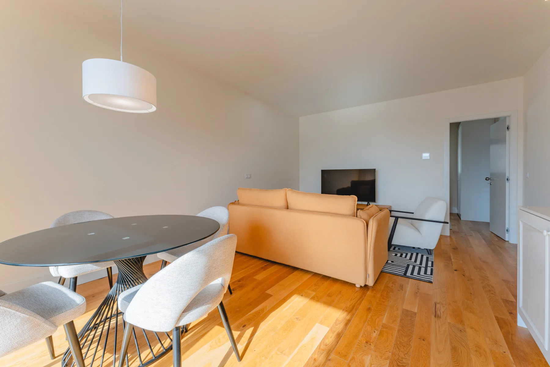 Sala de estar y comedor con un sofá beige, una mesa y suelo de madera.