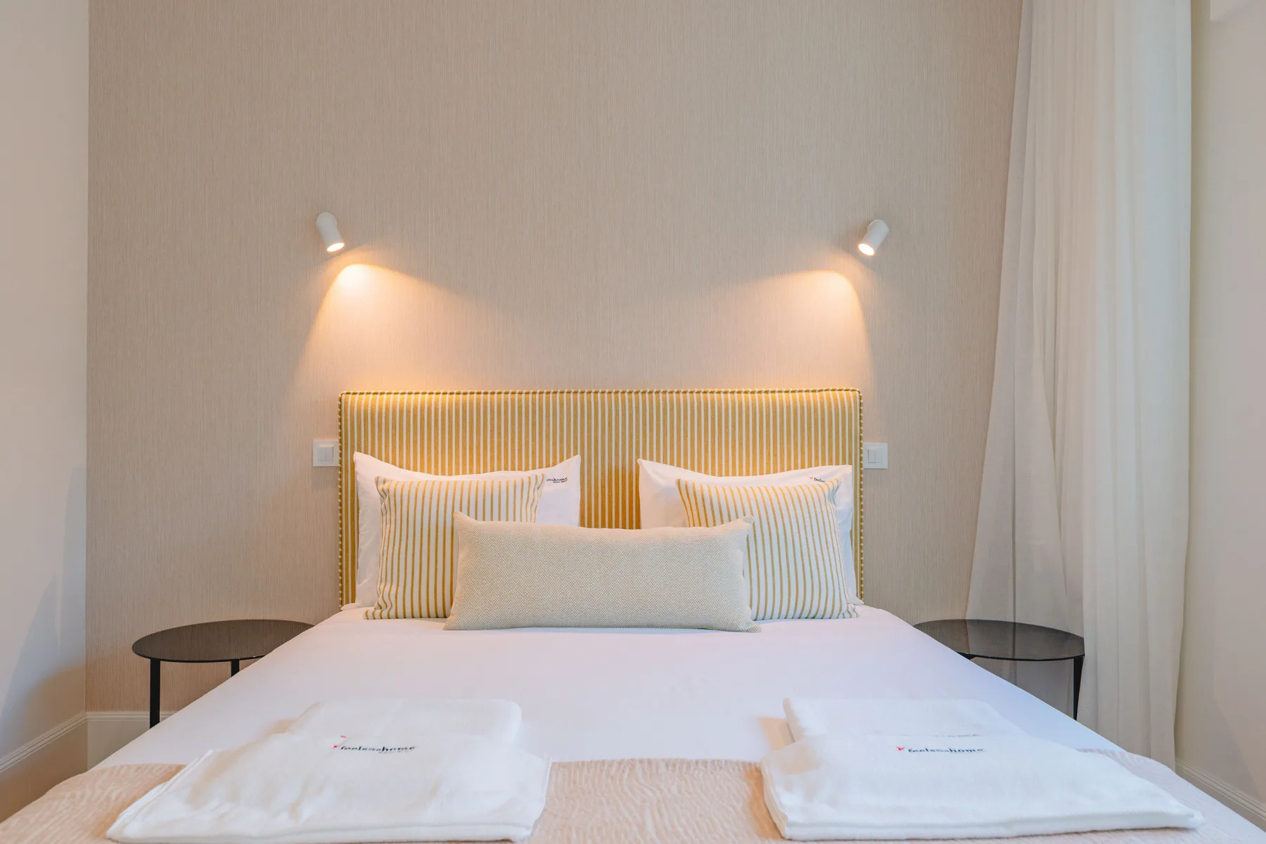 Dormitorio con un cabecero a rayas y dos luces de pared sobre la cama.