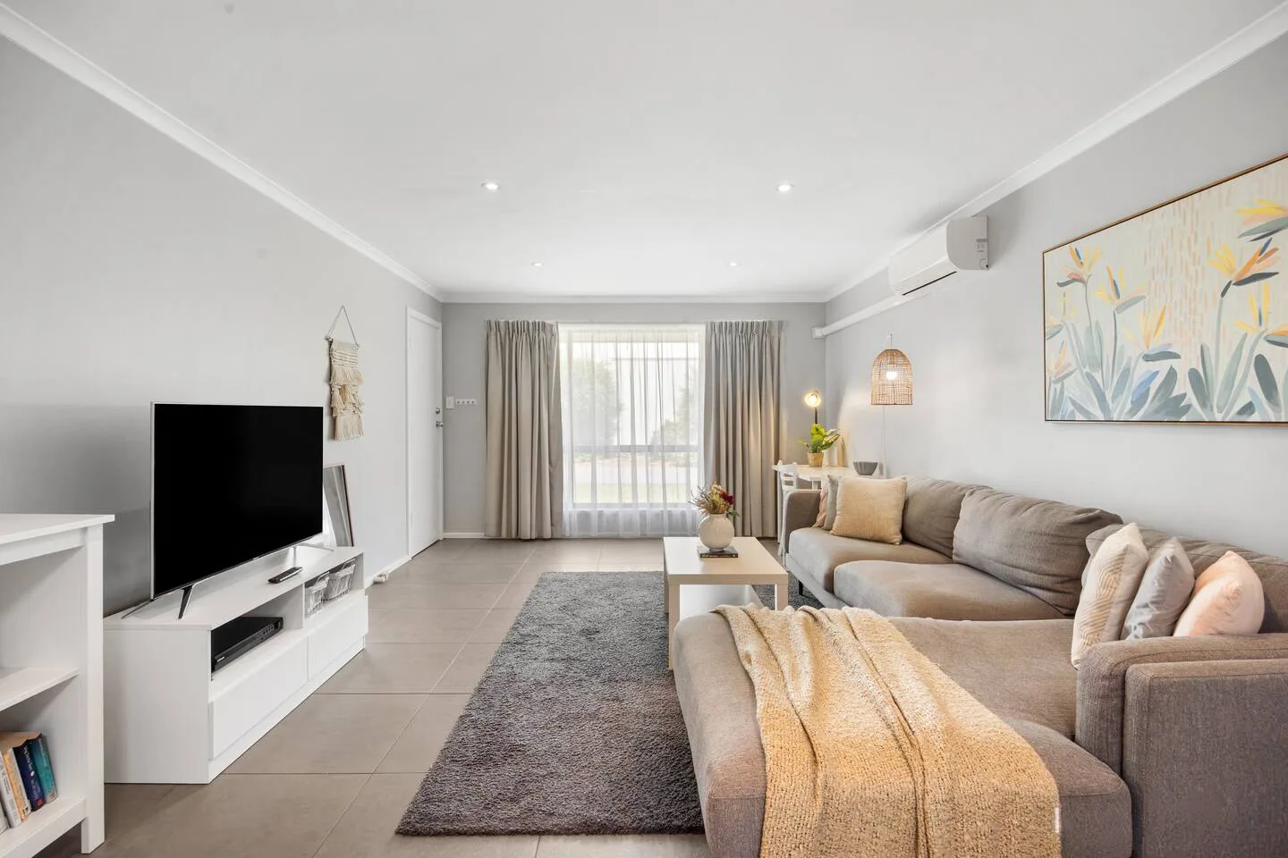 Una luminosa sala de estar con sofá seccional, televisor y una gran ventana con cortinas.