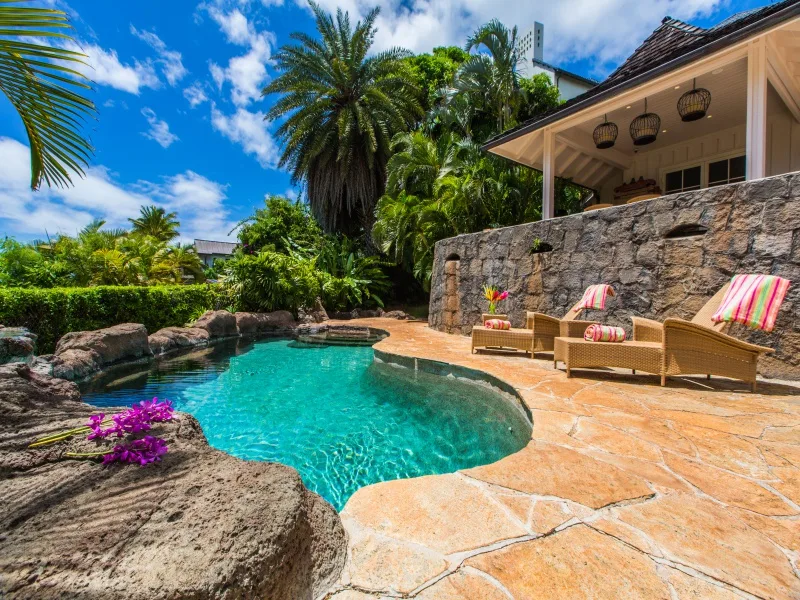 Una piscina está junto a un muro de piedra y asientos al aire libre, rodeada de vegetación tropical.