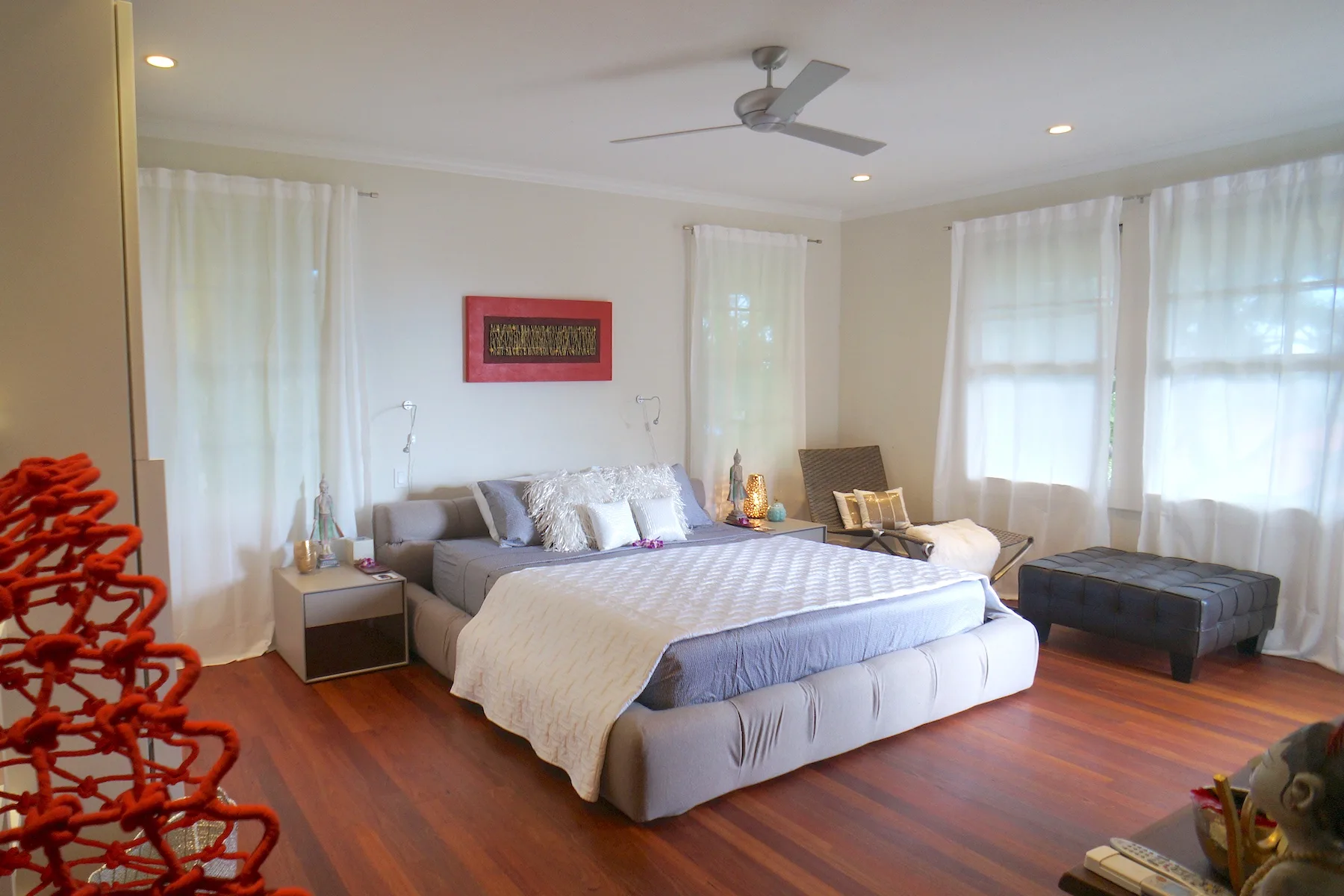 Un dormitorio luminoso con una cama grande, una mesita de noche y ventanas altas.