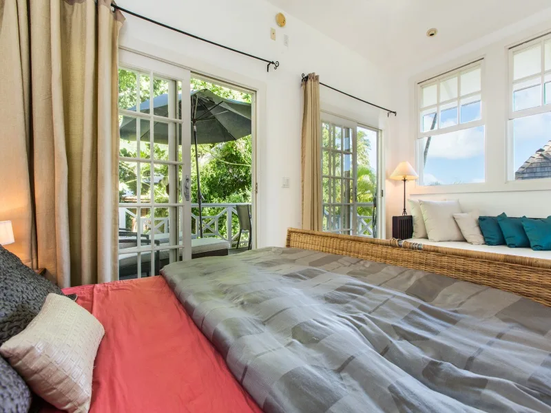 Un dormitorio luminoso con una cama grande y ventanas altas con vistas a la vegetación.