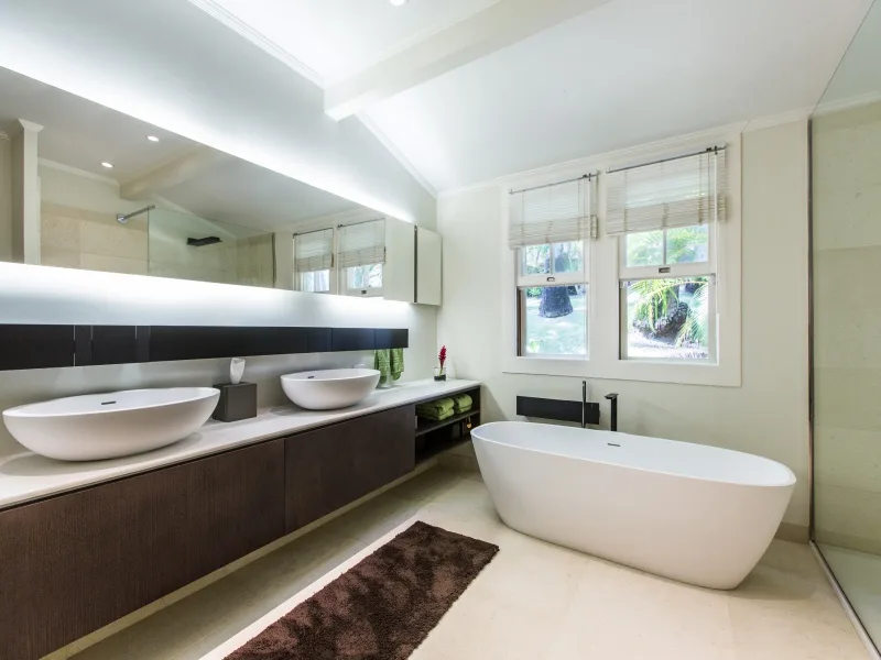 Un baño luminoso con un mueble largo, dos lavabos y una bañera exenta.